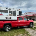 A red half-ton truck with a modified camper in the box and "Steffes Auctioneering" logos and URL on it. The camper has windows in it that allows an auctioneer to conduct business in all weather.