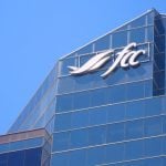 Looking skyward toward the top of the Farm Credit Canada building in Regina, Saskatchewan, with the company's stylized "FCC" logo on it against a clear blue sky.