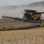 A yellow combine kicks up plenty of dust as it harvests a crop.