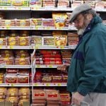 A bearded middle-aged man wearing glasses and a tam-style hat picks up a package of wieners in a WalMart grocery store.