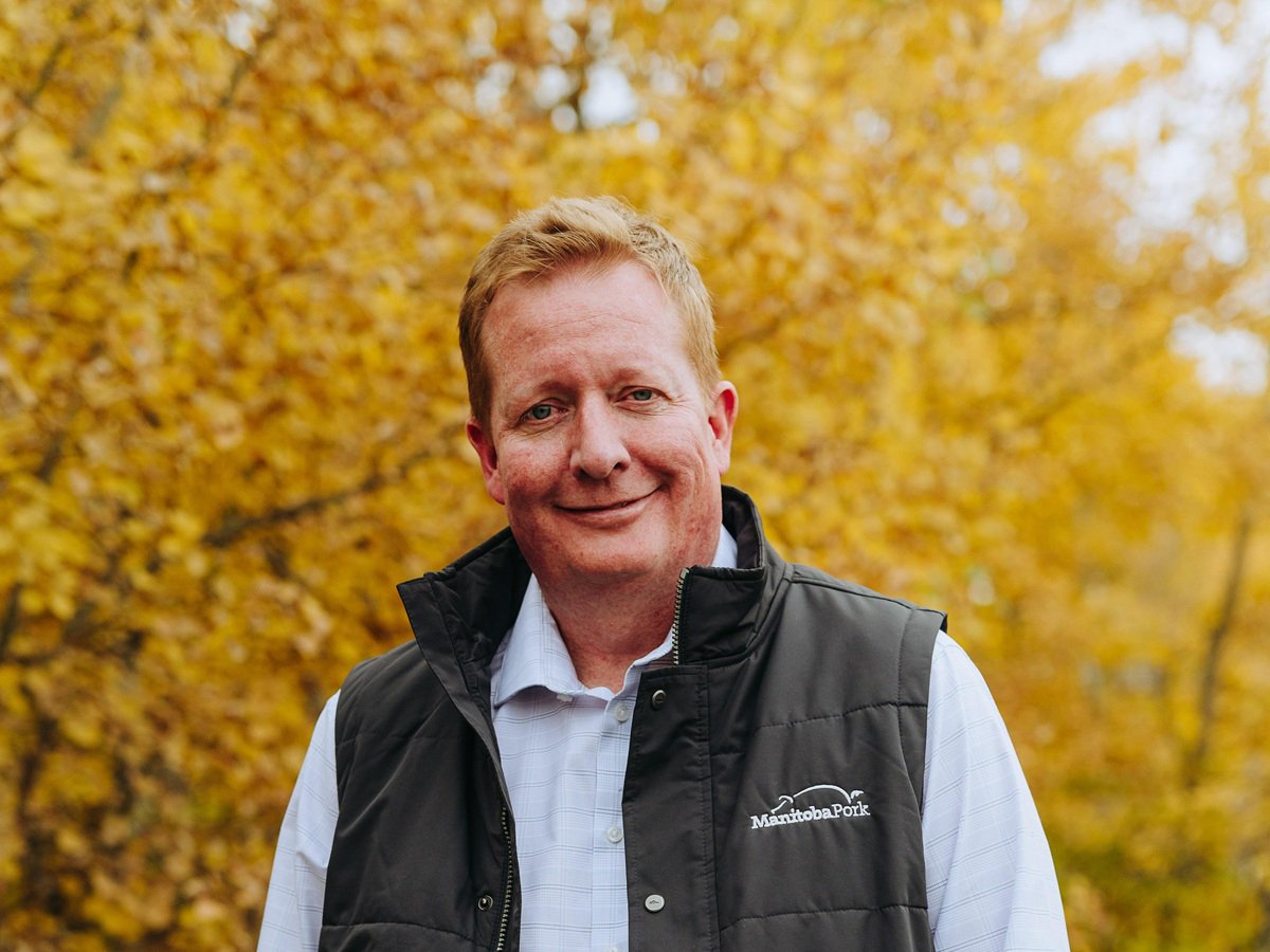 Grant Melnychuk, Manitoba Pork director of sustainable development, research and data management, stands in front of some trees with golden leaves wearing a Manitoba Pork vest.