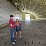 A man in a ball cap and a woman stand in a potato storage bin that has yellow spray foam insulation on its walls and curved ceiling.