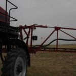 Close-up of the boom of a parked sprayer with a wind sock in the background on a cloudy day.