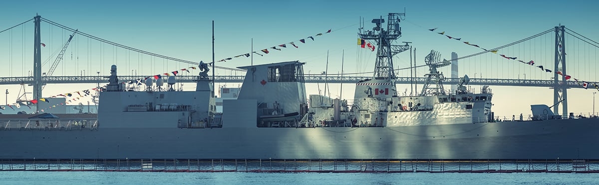 A Canadian Military warship is bathed in sunlight reflected off Purdy's Wharf Towers with the Angus L. MacDonald Bridge in the background.