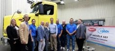 A group of men and women stand in front of a large yellow truck next to a sign with a red, oval Peterbilt logo on it that reads (in french) "1st model 567 Made in Canada 24 September 2025."