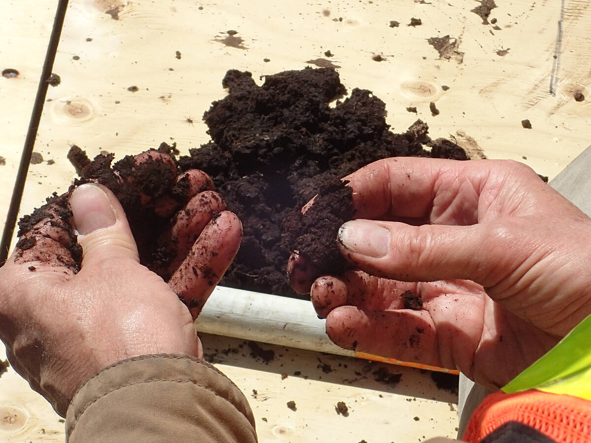 A close up of two hands rubbing dark soil between both thumbs and fingers as if to gain a sense of its texture.