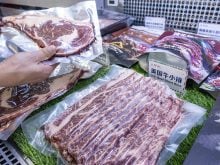 A hand holds a vacuum-packed steak above a meat display in a grocery story with a sign written in Chinese characters, subtitled in english below, "U.S. beef short ribs."