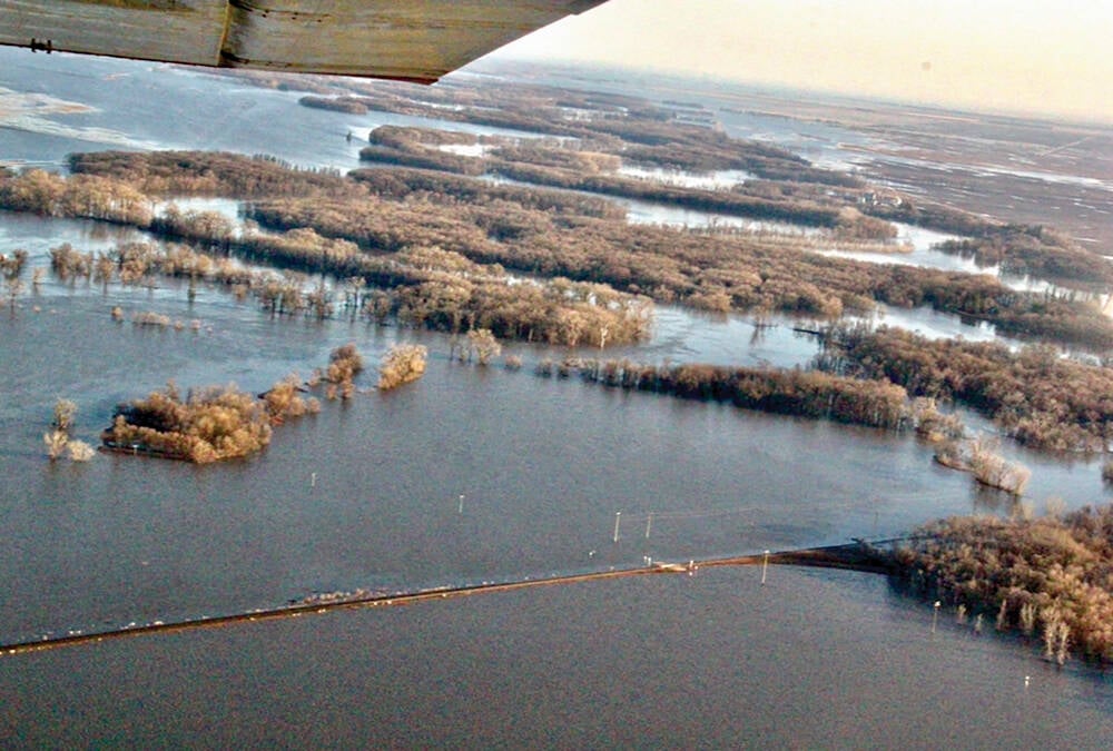An aerial view of flooding in Manitoba in 2022 that shows a rural grid road just barely above the surface of water on both sides of it.