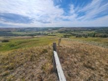 A view of a lush green valley looking overtop a barbed wire fence on a partly cloudy day.