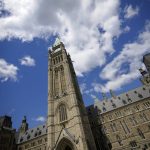 A view of the Peace Tower on Parliament Hill looking upward with a blue sky and a few clouds in the background.