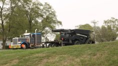 A Fendt Ideal combine sits on the trailer of a truck with a yellow "Oversize Load" banner on it.