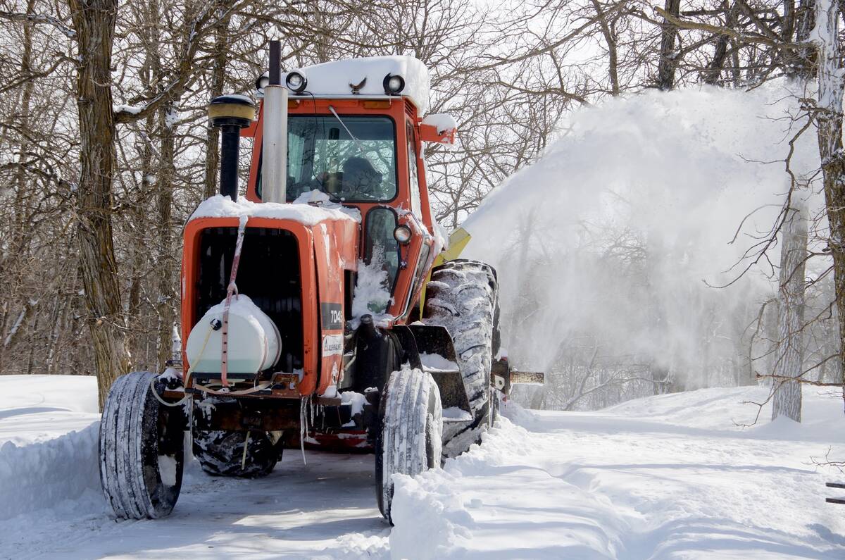 A farmer in central Manitoba blows snow out of his driveway with a tractor-mounted snowblower after a major winter storm.