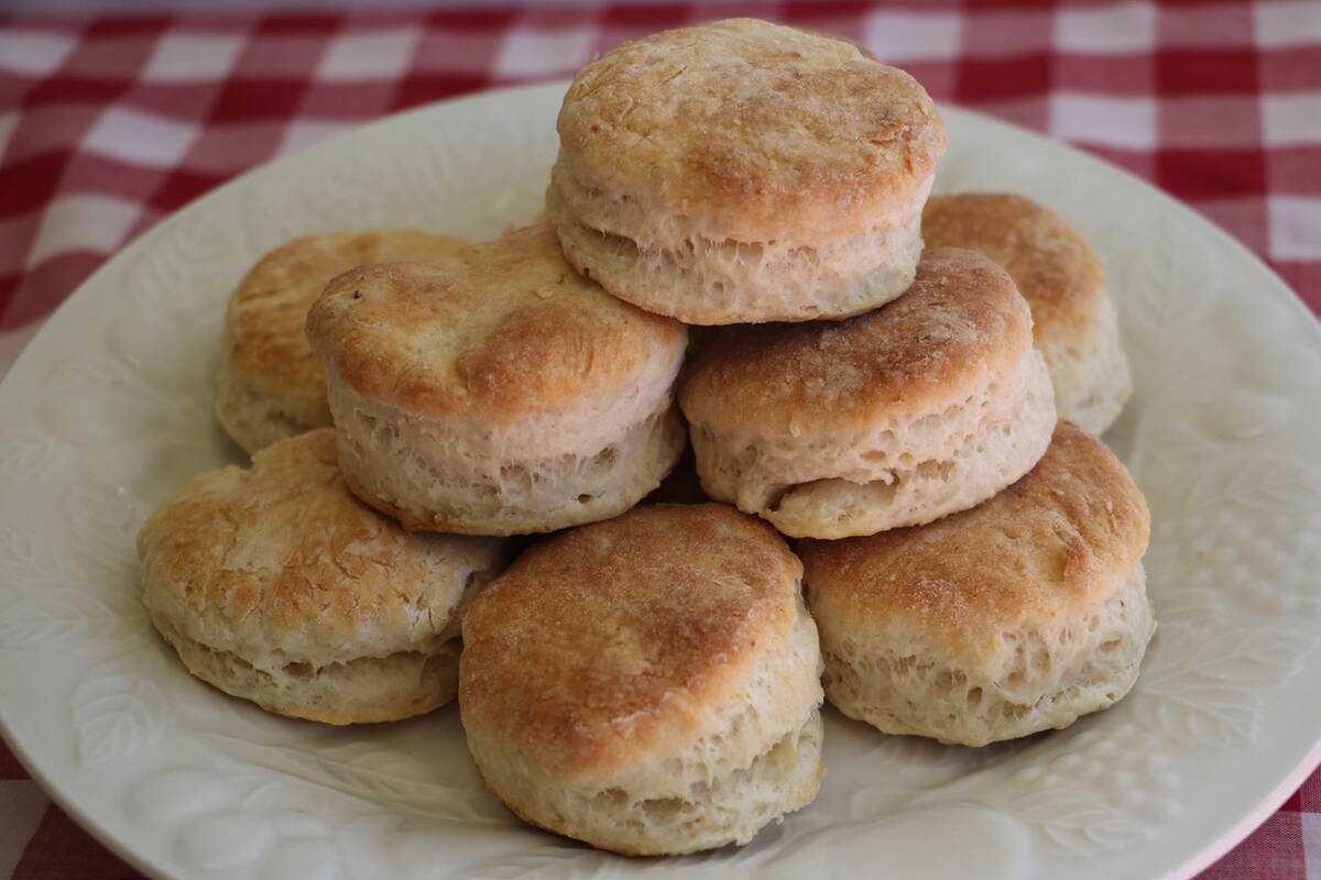 Baking powder biscuits are stacked on a white plate sitting on a red and white checkered tablecloth.