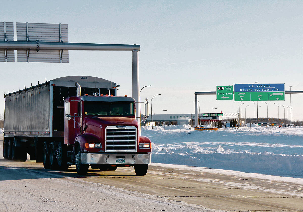 A grain truck drives under highway signs for the U.S. border in winter.