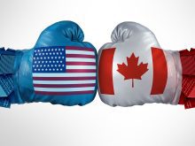 A photo illustration showing two boxing gloves touching, as boxers do at the beginning of a fight, with one glove having a U.S. flag on it and the other a Canadian flag.