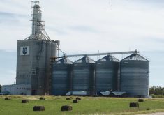 A Parrish & Heimbecker inland terminal with two grain trucks parked beside it in the summer time.