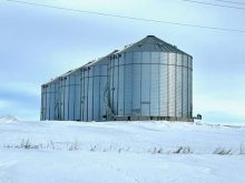 Four massive round, steel grain bins outside of Russell, Manitoba, with snow on the ground around them..