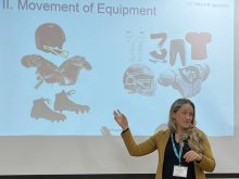 Veterinarian Dr. Alycia Webster of Telus Agriculture stands on a stage gesturing toward a large screen as she talked about biosecurity at the MNP Ag Connections Conference in Medicine Hat, Alberta, in November 2025.