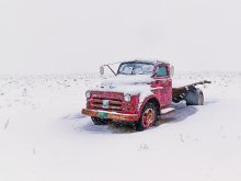 An old, red flatbed truck parked and surrounded by snow.