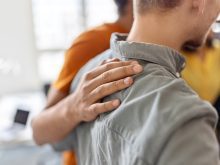A man places his hand on the back of another in an act of support.