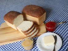 Fresh bread is sliced and sitting on a bread board with a small plate with a block of butter and a butter knife on it nearby.
