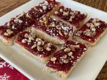 A tasty looking pastry with jam, crushed nuts and a sprinkle of icing sugar on top.