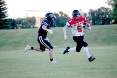 One football player chases another on a grass field.