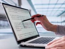 An editor uses a stylus to make edits to a document visible on the screen of a laptop computer.
