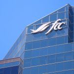 A photo looking upward at the top of blue, glass-covered building with the stylized "FCC" logo on it for Farm Credit Canada.