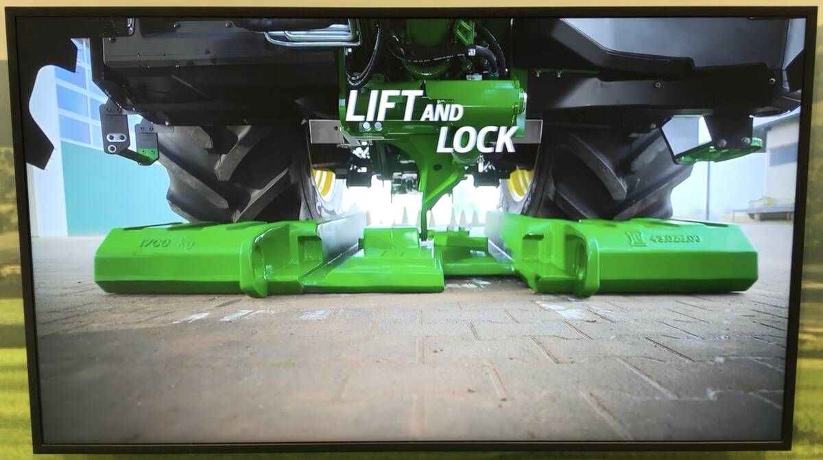 A screen grab from a promotional video for the EZ Ballast catching arm showing it attaching to a weight before it lifts it up to the tractor&rsquo;s undercarriage. 
