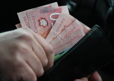 Close-up of a man's hand removing a number of $50 bills from a leather wallet.