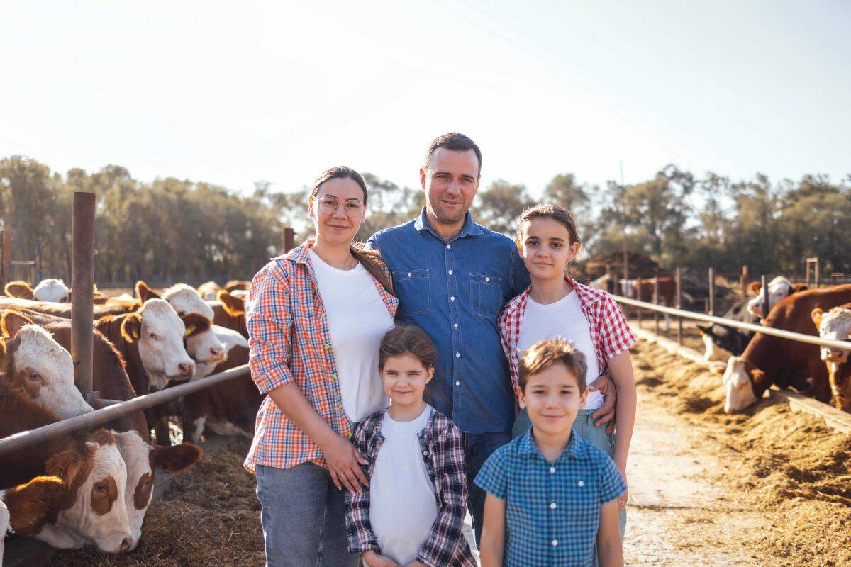 A wife, her husband, and three children pose for a phot in an alleyway between two cattle pens, both full of cattle.