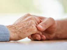 Close-up of an elderly, frail hand being held by a younger, strong-looking hand.