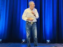 Mike Doliniski stands on a stage addressing an unseen audience.