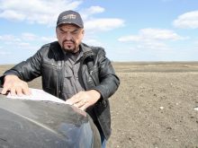 Major Saskatchewan landowner Robert Andjelic looks at a map spread open on the hood of his truck on a sunny day with the an unplanted field behind him.