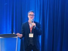 Sylvain Charlebois, an agricultural economist, stands on a stage next to a podium speaking into a microphone at the Convergence agricultural conference in Regina Saskatchewan.
