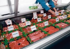 A worker in a meat store adjusts the labels on some of the meat on display in a large refrigerated display case.