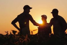 Three people meeting and shaking hands in a field, silhouetted against the setting sun.