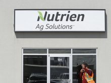 A "Nutrien Ag Solutions" sign above a glass door with a man in a safety vest walking in front of it.