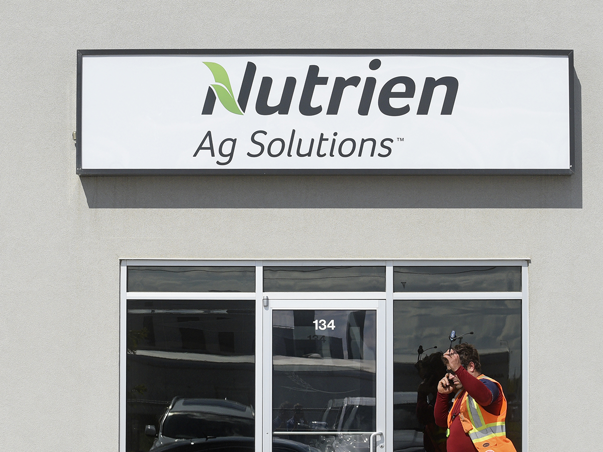 A "Nutrien Ag Solutions" sign above a glass door with a man in a safety vest walking in front of it.