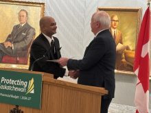 Two men shaking hands at a podium with a Government of Saskatchewan "Protecting Saskatchewan" sign on it.