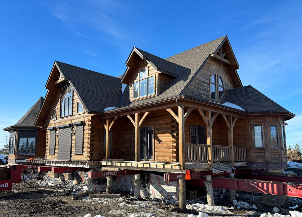 A large, log-style 2-storey home sits on steel beams up off the ground ready to be moved.