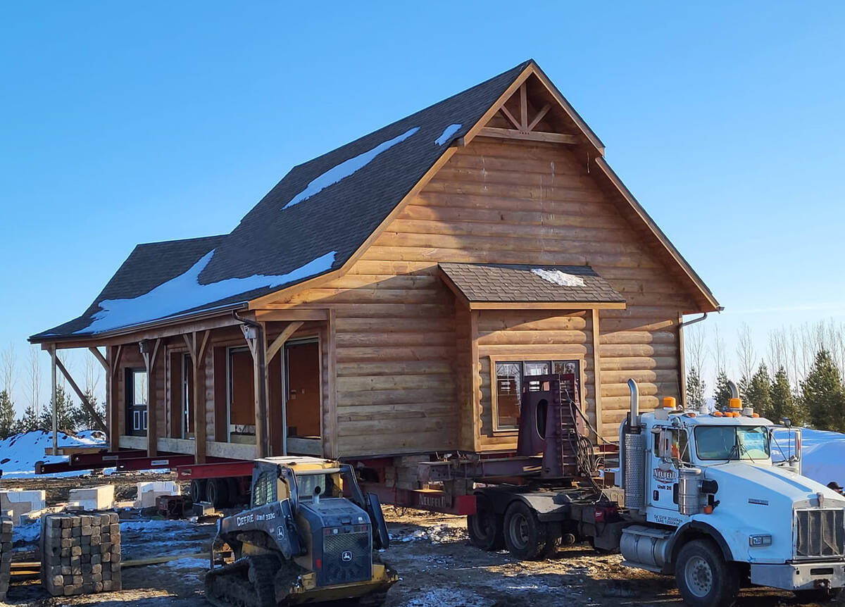 A two-storey, log-style garage sits on steel beams off the ground and already attached to a large truck, ready to be moved.
