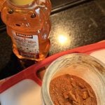 Looking down from above at a container of honey shaped like a bear and a round plastic container of reddish powder.