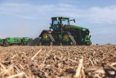 A large, tracked John Deere tractor pulls an implement through a field covered in litter.