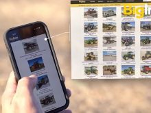 A man's hand holds a smartphone scrolling with his left thumb over items up for auction on an auction website. The same website is seen on a laptop computer to the right of the smart phone.