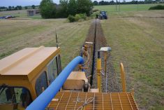 A trenching machine carves a trench into a field running blue plastic tile drainage piping into the trench simultaneously.