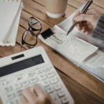 Close-up of the hand of a woman holding a pen over some receipts in her right hand while punching numbers into a calculator with her left hand.