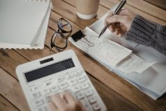 Close-up of the hand of a woman holding a pen over some receipts in her right hand while punching numbers into a calculator with her left hand.