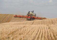 A tractor pulling an air seeder has just come over a hill in a stubble field.